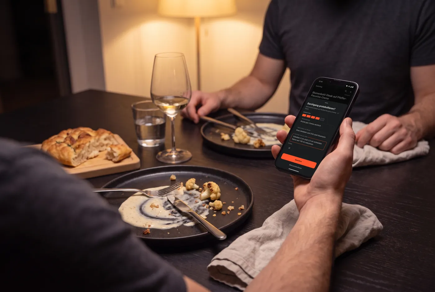At the table after dinner: a hand holds the phone with the cooking log of Cook & Repeat above the empty plates.